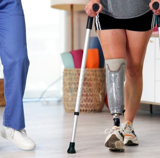 Ilustracja pokazuje naukę chodzenia w protezie nogi przy użyciu kul w asyście rehabilitanta