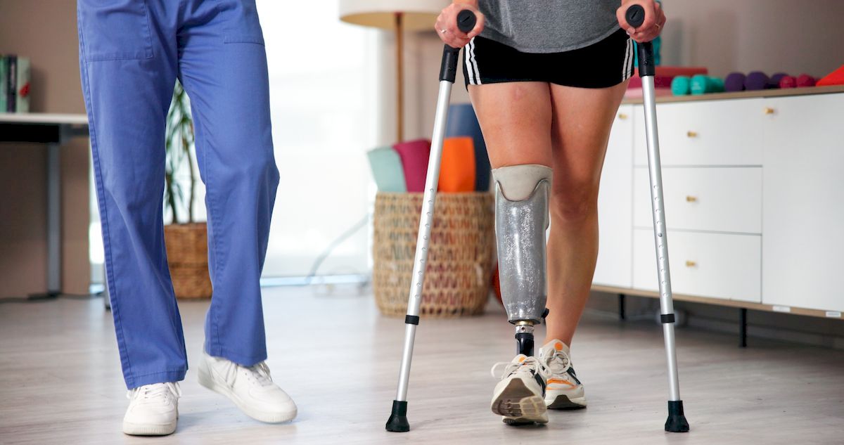 Ilustracja pokazuje naukę chodzenia w protezie nogi przy użyciu kul w asyście rehabilitanta